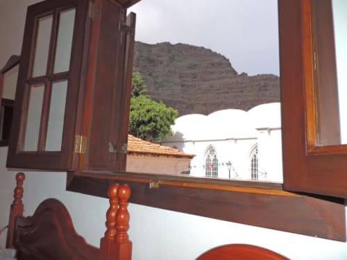 Vista a través de puertas de madera de la capilla blanca y la montaña volcánica desde el balcón del estudio de Casa Rural Los Helechos en Agulo