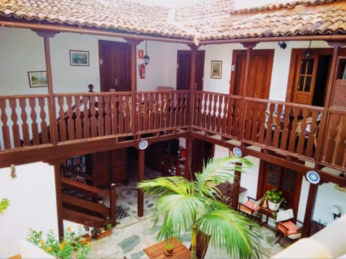Patio de estilo colonial en Casa Rural Los Helechos en Agulo con barandillas de madera, tejado de barro y exuberantes plantas de palma