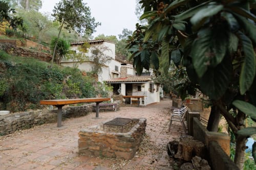 Patio rústico en Masías Can Trabal, Olerdola: edificio encalado, bancos y exuberante vegetación