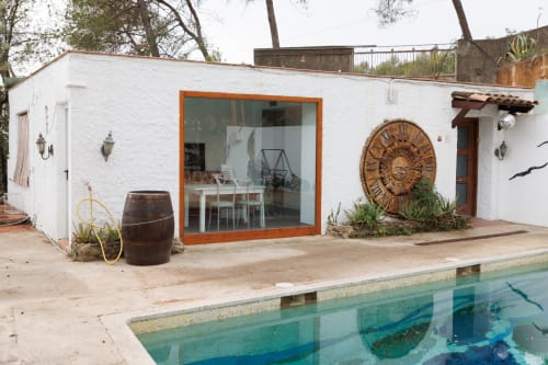 Terraza junto a la piscina de Masias Can Trabal con edificio blanco, ventanas con marco naranja y decoración vintage en Olerdola