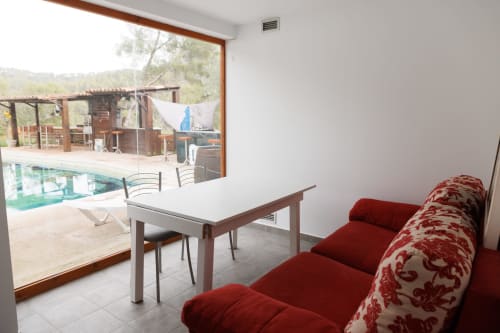 Elegante sala de estar con sofá rojo estampado con vistas a la piscina en Masias Can Trabal, Olerdola
