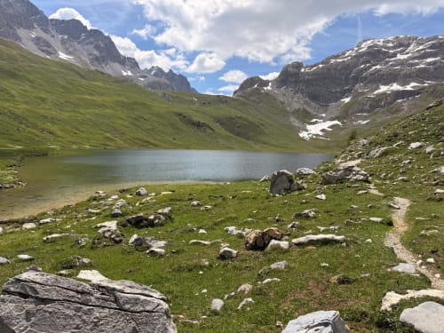 Lac alpin entouré de prairies verdoyantes et pics rocheux près de l'hôtel L'Alp'In à La Plagne Tarentaise