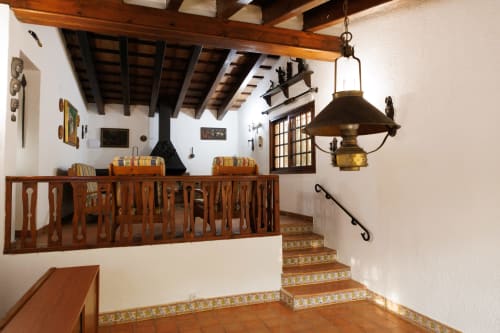 Escalera rústica en Masías Can Trabal con vigas de madera, baldosas de terracota e iluminación colgante de latón