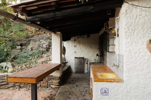 Rústica zona de patio cubierto en Masías Can Trabal con banco de madera, muros de piedra blanca y suelo de barro cocido en Olerdola