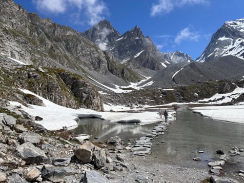 Lac alpin avec plaques de neige, montagnes rocheuses et randonneurs près de L'Alp'In à La Plagne Tarentaise
