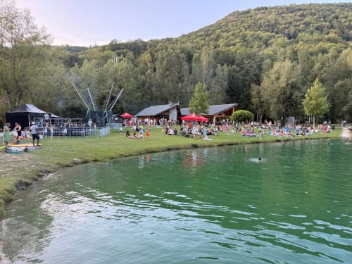 Les clients de l'Alp'In profitant d'un festival en plein air au bord de la rivière à La Plagne Tarentaise avec les montagnes boisées en arrière-plan