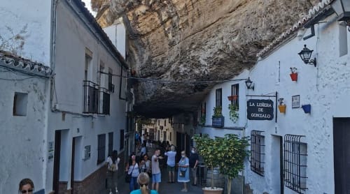 Calle de casas cueva en Setenil de las Bodegas con edificios blancos construidos bajo saliente rocoso, turistas explorando La Joya de