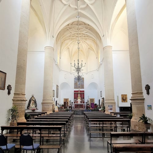 Interior de iglesia gótica con bóvedas de cañón, bancos de madera y altar en Setenil de las Bodegas