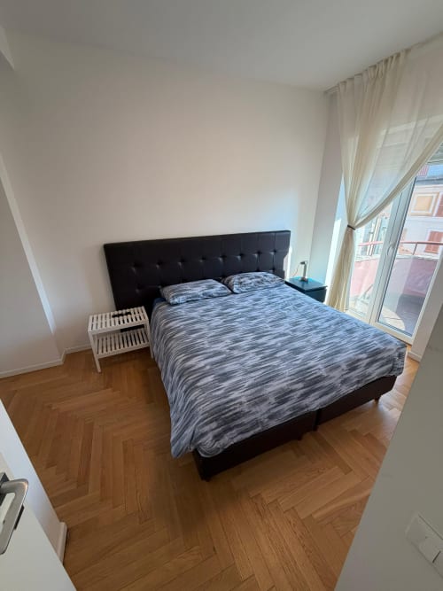 Camera da letto moderna in appartamento milanese con letto queen, testiera nera, parquet a spina di pesce, vista sulla città e accesso alla terrazza