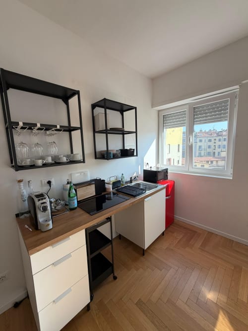 Cucina di moderno appartamento milanese con scaffalature in metallo nero, piano di lavoro in legno, armadi bianchi e vista sulla città dalle finestre
