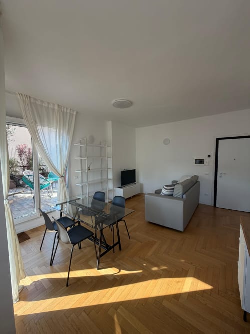 Soggiorno di un moderno appartamento a Milano con tavolo da pranzo, divano, TV e accesso alla terrazza