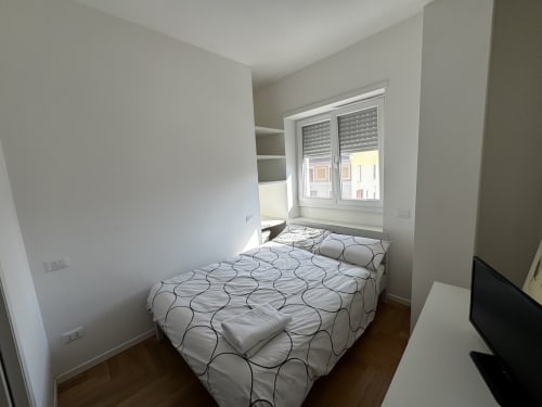 Camera moderna della Porta Romana Suite Milano con letto, finestra sulla città, scaffalature e pavimento in legno
