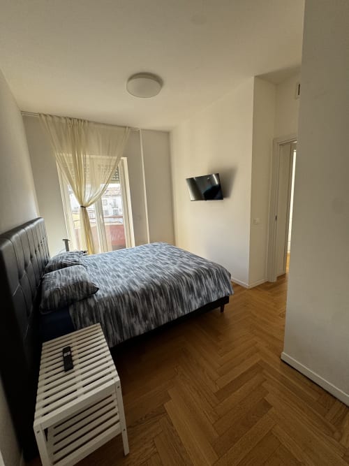 Camera moderna della Porta Romana Suite Milano con letto matrimoniale, TV a parete, pavimento in legno e balcone con vista sulla città