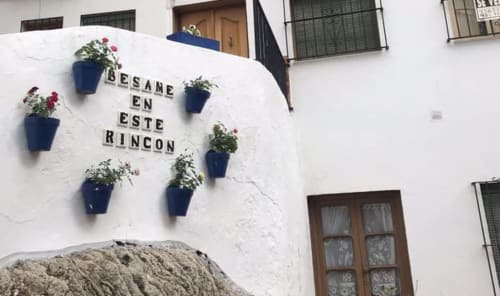 Pared encalada en La Joya de Setenil con macetas azules y letrero 'Besame en este Rincón'