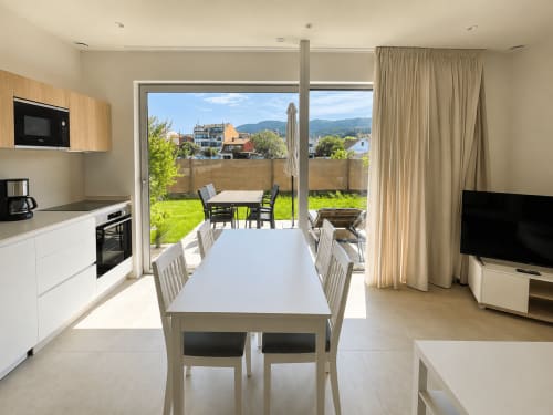 Moderno apartamento en Baiona con cocina abierta, comedor y vistas al jardín a través de amplias puertas de cristal