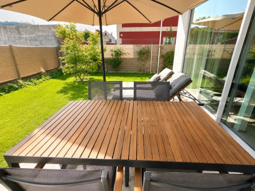 Terraza soleada con tarima de madera, muebles de patio, sombrilla y jardín cuidado en Holibai ModulSuites en Baiona
