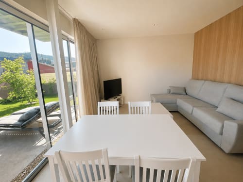 Moderna sala de estar en Baiona con mesa de comedor, sofá gris, TV y acceso a terraza con vistas al jardín