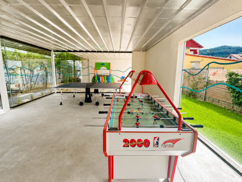 Sala de juegos cubierta en Holibai Baiona con futbolín, ping pong y casita infantil colorida con vistas al jardín