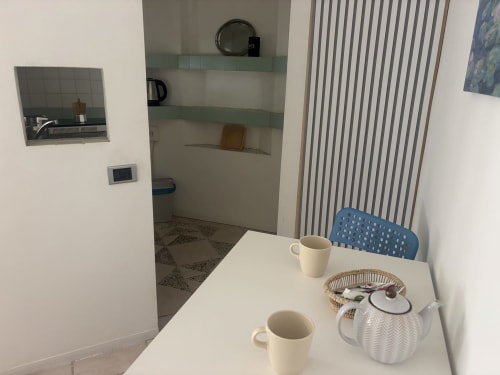 Zona cucina Lovelyloft Milano con tavolo bianco, tazze, teiera e sedia blu accanto al cucinino con scaffalature