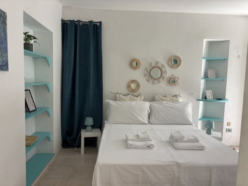 Lovelyloft Milano bedroom with turquoise shelving, white bedding, dark curtains and decorative wall mirrors