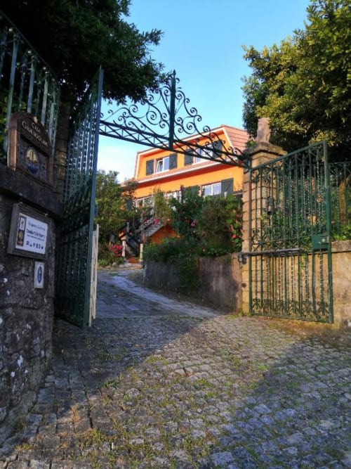 Verziertes Schmiedeeisen-Tor am Eingang der Herberge Bom Caminha in Caminha, Portugal, mit gelbem Gebäude und efeubedeckten Wänden