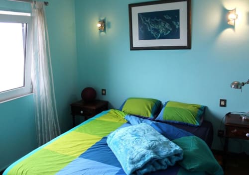 Bright turquoise bedroom at Bom Caminha hostel in Caminha with lime green and blue bedding, matching pillows, and framed