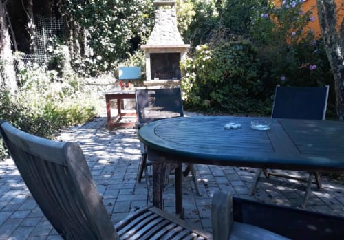 Bom Caminha hostel patio with dining table, chairs, fireplace, and lush greenery in Caminha, Portugal