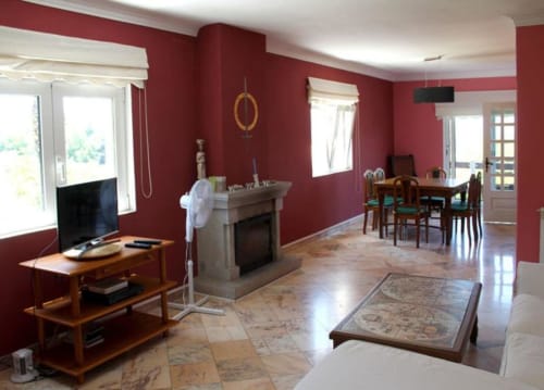 Bom Caminha hostel common room in Caminha with red walls, fireplace, dining table, TV, and wooden flooring