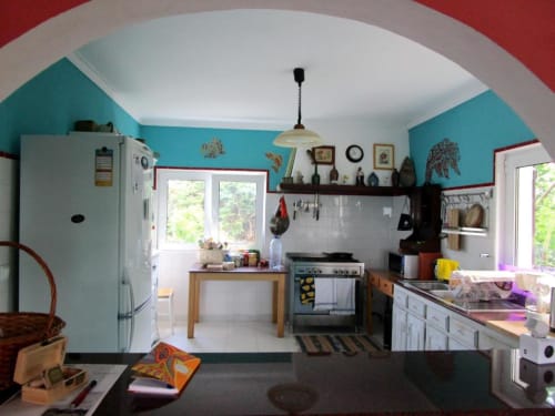 Colorful hostel kitchen at Bom Caminha with turquoise walls, white appliances, and bright red accents