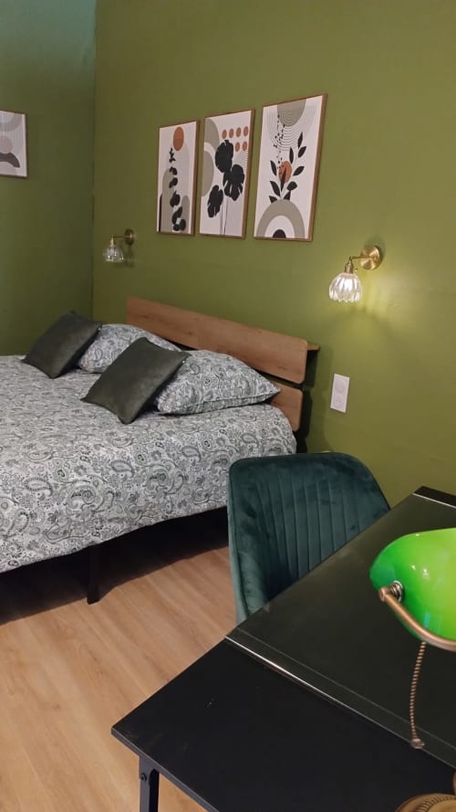 Chambre moderne aux Troglos de Beaulieu avec murs vert anis, lit en bois, literie à motifs et art botanique mural