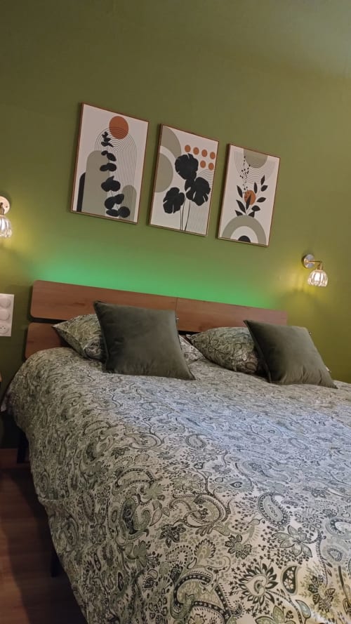 Chambre moderne aux Troglos de Beaulieu avec murs vert olive, lit en bois, literie à motifs et trois tableaux abstraits