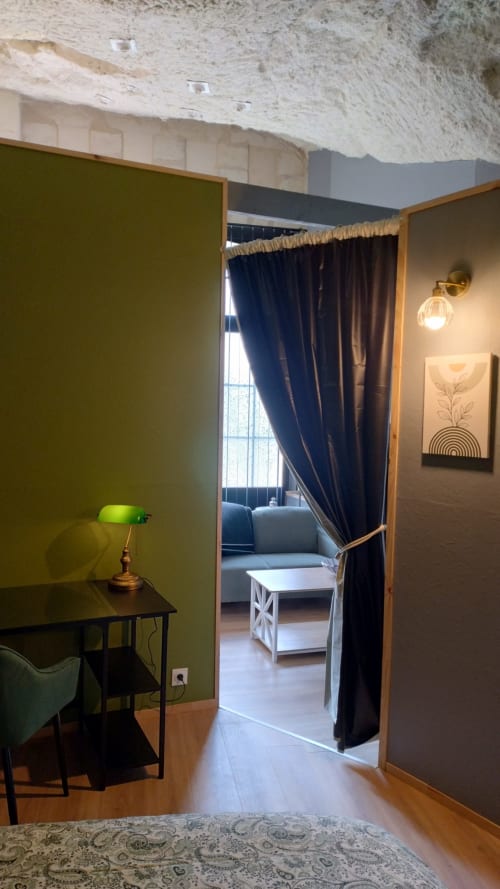 Chambre moderne aux Troglos de Beaulieu avec murs vert olive, bureau en bois avec lampe de banquier verte, accès ouvert vers