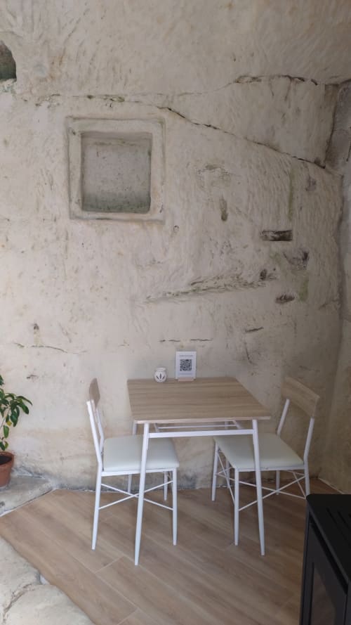 Petit coin repas rustique dans la chambre troglodyte des Troglos de Beaulieu avec table en bois, chaises blanches et murs en pierre