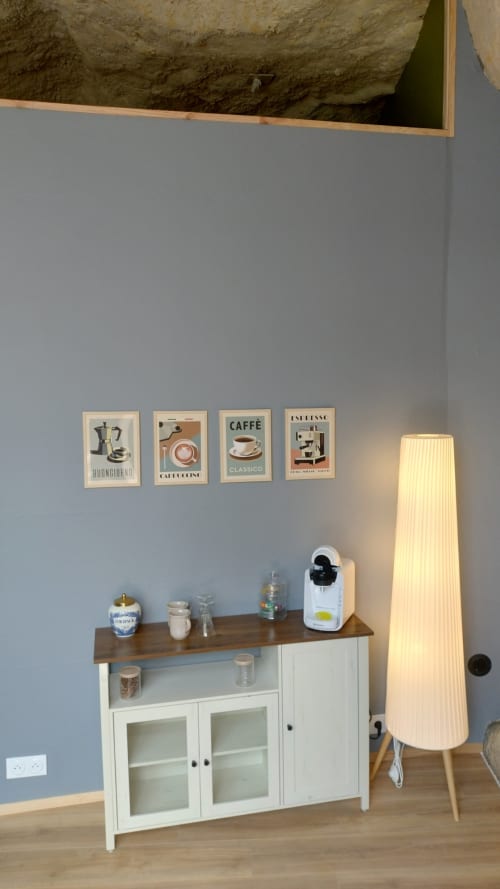 Coin café aménagé dans la chambre de l'hôtel Les Troglos de Beaulieu avec affiches de café italiennes encadrées, meuble blanc et lampadaire