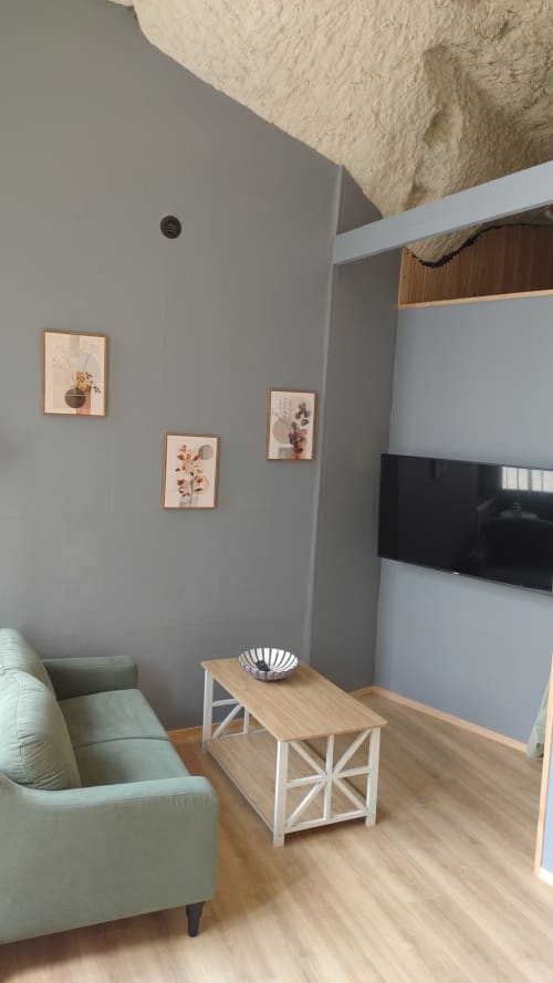 Espace de vie moderne dans la chambre La Cave 1872 aux Troglos, avec fauteuil vert, table en bois, art mural et télévision écran plat