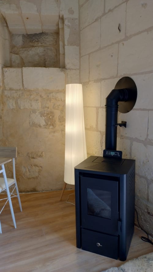 Poêle en bois noir avec tuyau de cheminée et lampadaire blanc dans une chambre en pierre rustique aux Troglos de Beaulieu, Beaulieu-lès-Loches