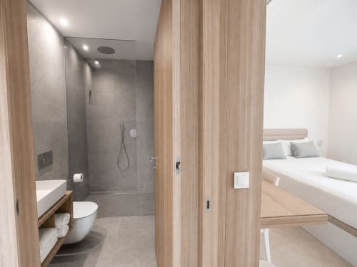 Baño en suite moderno con ducha a ras de suelo y detalles en veta de madera en apartamento premium de Holibai, Baiona