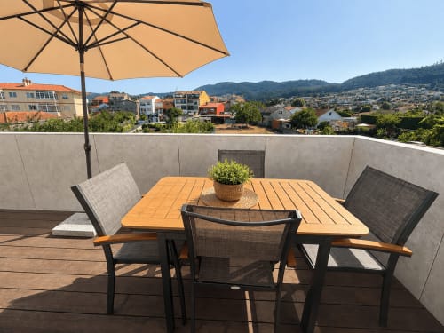 Terraza soleada del apartamento ModulSuites en Baiona con mesa de comedor, sombrilla y vistas a la ciudad y montaña