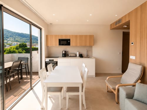 Cocina y comedor modernos en Holibai, Baiona, con vistas a la ciudad, mesa blanca, muebles de madera y acceso a