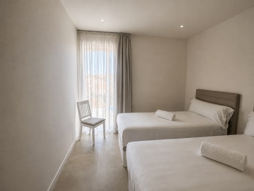 Habitación moderna en Holibai, Baiona, con dos camas, vista a la ciudad a través de ventanales y mobiliario contemporáneo