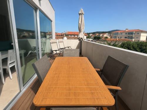 Terraza en la azotea de ModulSuites Baiona con mesa de comedor de madera, tumbonas y vistas de la ciudad de Baiona, España