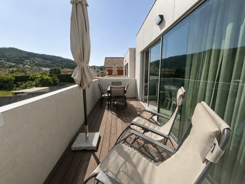 Terraza moderna del apartamento Holibai Baiona con tumbonas, mesa de comedor, sombrilla y vistas a las montañas