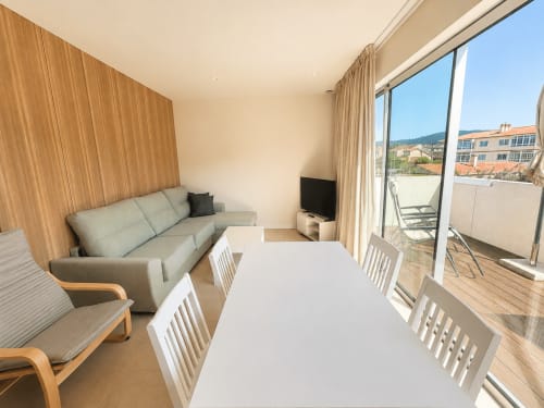 Moderno salón de apartamento en Baiona con mesa de comedor, sofá gris, televisor y terraza con vistas a la ciudad
