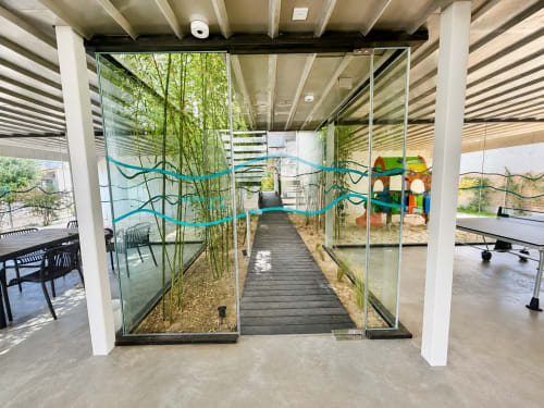 Terraza cubierta moderna del hotel Holibai en Baiona con mamparas de cristal, arte de olas azules, plantas de bambú y área infantil