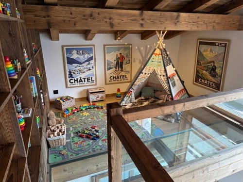 Mezzanine chaleureuse pour enfants dans chalet de montagne avec tipi, jouets, affiches vintage de Châtel, poutres en bois