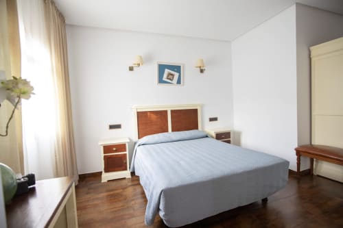 Espacioso dormitorio doble en Hostal Atalaya con ropa de cama azul, cabecero de madera, mesillas color crema y pisos de madera