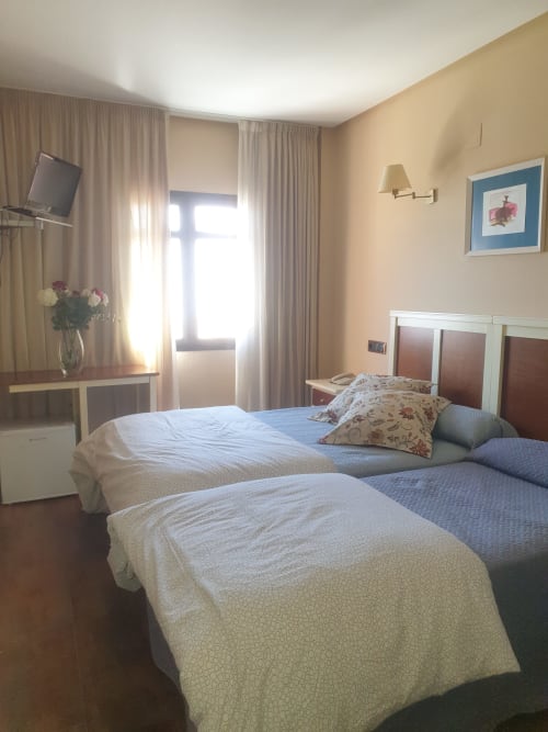 Habitación triple en Hostal Atalaya de Minas de Ríotinto con dos camas, televisor y ventanas luminosas