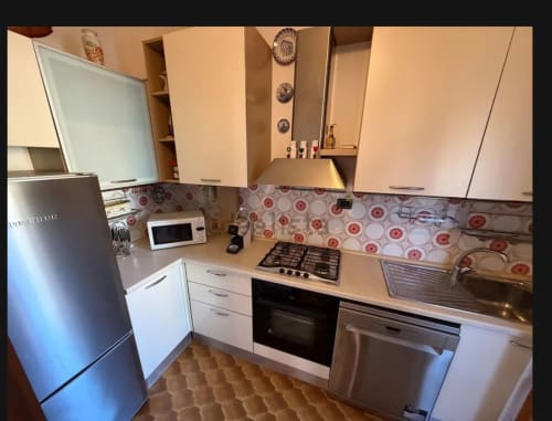 Cucina moderna nell'appartamento di Cervia con mobili bianchi, elettrodomestici in acciaio inox, piastrelle rosse tonde e piano cottura a gas