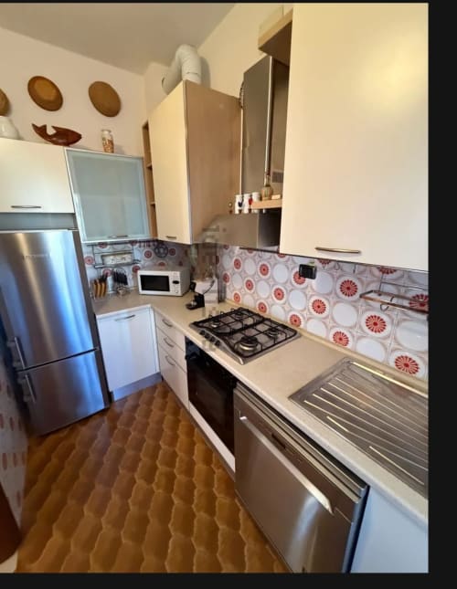 Cucina moderna con piano cottura a gas, elettrodomestici in acciaio inox e piastrelle rosse decorative nell'appartamento di Cervia