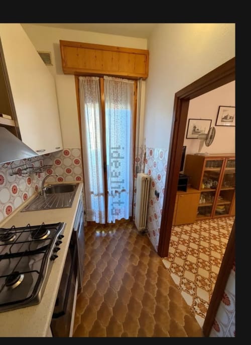 Cucina dell'appartamento a Cervia con fornello a gas, lavello, rivestimento decorato e porta aperta sulla zona living